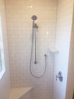 Opposite shower wall featuring adjustable shower wand, another custom quartz shelf and shower seat.