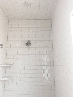 Subway tile inside shower installed on walls as well as ceiling with inset can lighting.