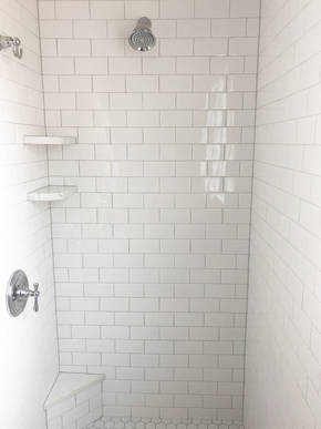 Inside of shower featuring subway tile and custom quartz shelves with footrest to match vanity countertop.